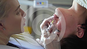 Vertical shot of Beautician doctor makes botox injection in the lips of young beautiful woman. Extreme close up 4k shot