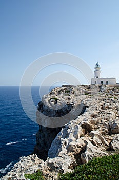 Vertical shot of a beautiful white lighthouse at the edge of a cliff in Menorca island, Spain