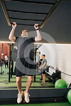 Vertical shot of beginner sportsman doing pull-ups on horizontal bar at gym. Sports male workout exercising. Fit and