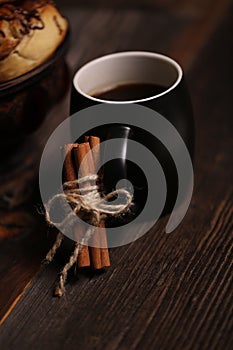 Vertical shot of a black tea mug near some cinnamons and a vase with tasty biscuits