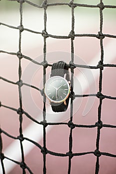 Vertical shot of a black watch hanging on a tennis net