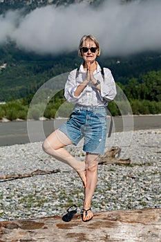 Vertical shot of a blonde female in jean shorts doing yoga on a log