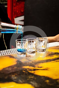 Vertical shot of a blue drink being poured into a glass on the bar stand