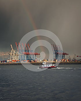 Vertical shot of a boat in the water with a rainbow in the sky