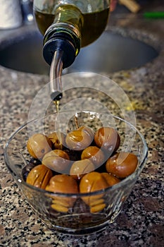 Vertical shot of a bottle of olive oil pouring onto green olives in a bowl
