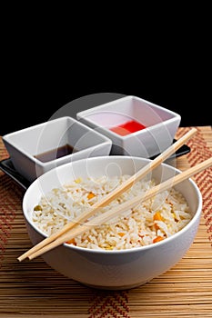 Vertical shot of a bowl of cooked rice with chopsticks on it on the table with sauces