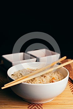 Vertical shot of a bowl of cooked rice with chopsticks on it on the table with sauces