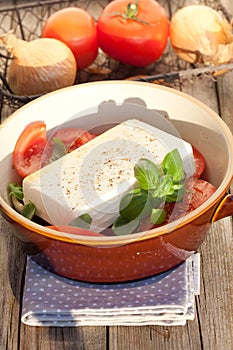 Vertical shot of a bowl of greek salad with tomatoes, basil, onion and feta cheese on a wooden table