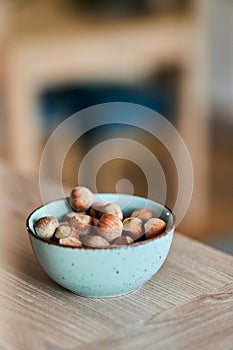 Vertical shot of a bowl of hazelnuts on a wooden table in a blurred background