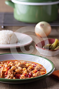 Vertical shot of a bowl of vegetable soup, a bowl of pickles and a plate of rice on a wooden table