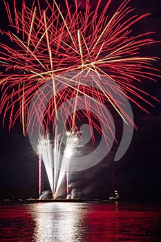 Vertical shot of bright red and white fireworks display over the water