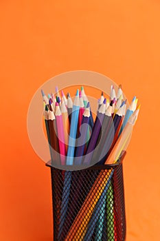 Vertical shot of a bunch of colorful pencils on metal holder isolated on orange background