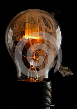 Vertical shot of a burning light bulb with smoke coming out of it isolated on a black background