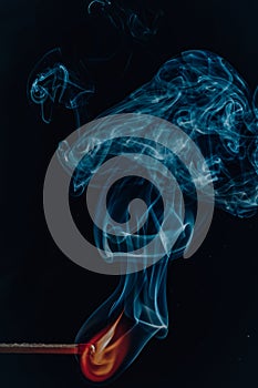 Vertical shot of a burning match with blue smoke clouds