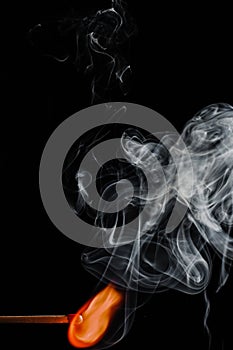 Vertical shot of a burning match with smoke clouds on a black background