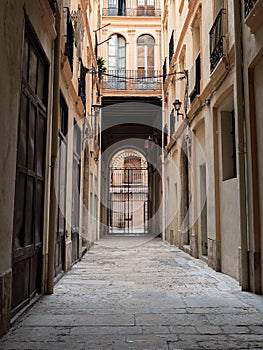 Vertical shot of a Callejon between old buildings with a gate at the end in Tortosa