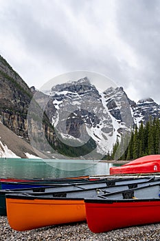 Vertical shot of canoes on the shore of Moraine Lake surrounded by snowy hills in Canada