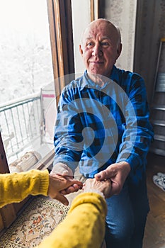 Vertical shot of caucasian elderly retired senior man happily holding his wife& x27;s hands by the window.