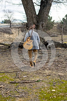 Vertical shot of a Caucasian white man with a gray coat and a guitar in the park