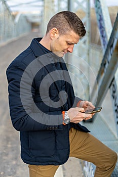 Vertical shot of a Caucasian white man on the smartphone on the bridge