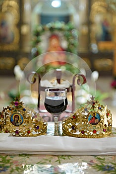 Vertical shot of the ceremonial crowns and a glass of wine as orthodox wedding accessories.