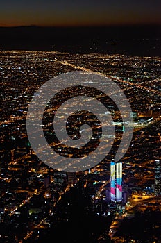 A vertical shot of the city of Bogota at dusk from Monserrate, with night lights and the Colpatria skyscraper on the lower side of photo