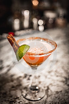 Vertical shot of a classic margarita cocktail with a slice of lime and salty rim on bar counter