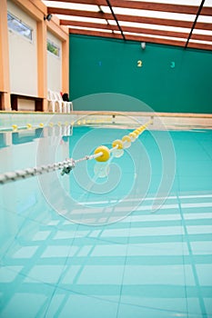 Vertical shot of a clean indoor gym pool full of water under sunlight with bulkheads dividing lanes