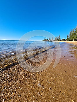 Vertical shot of a clear blue sky over a calm wavy sea with a sandy coastline