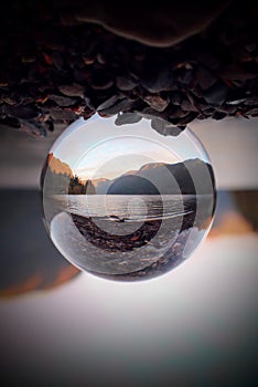 Vertical shot of a clear crystal glass ball on the rock of the lake scenery under mountains