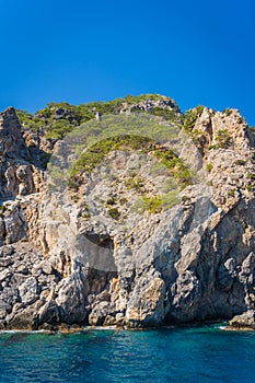 Vertical shot of a cliff with green plants on it on the Aegean Sea coast