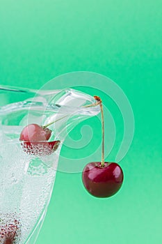 Vertical shot cold water with ice in the glass and pair of fresh cherries.