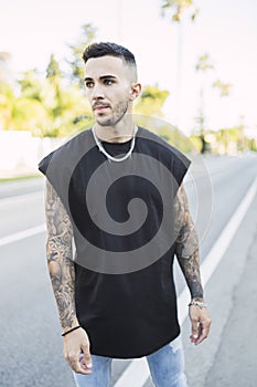 Vertical shot of a cool young man with tattoos wearing a black t-shirt standing on the street
