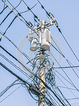 Vertical shot of a crowded electrical pole with cords on a clear blue sky background