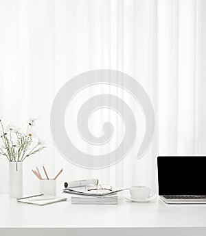 Vertical shot of a cup of coffee, a laptop,  a vase full of flowers, magazines on a white table