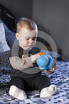 Vertical shot of cute fair baby girl sitting on bed examining duck toy