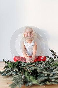 Vertical shot of cute lovely small girl sits crossed legs against white background, has happy expression, rejoices photo