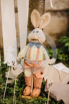 Vertical shot of a cute rabbit toy for the Easter leaned against a tree on the blurred background