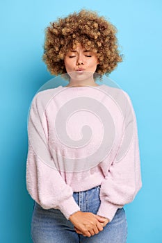 Vertical shot of cute young woman with curly Afro hair keeps eyes closed lips folded waits for kiss, dreams about