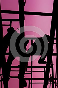 Vertical shot of a dark silhouette of construction workers against a pink sky in the background