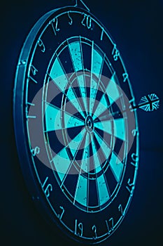 Vertical shot of a dartboard with a bullseye in the centre, illuminated by neon blue light