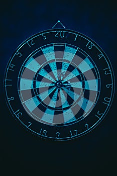 Vertical shot of a dartboard with a bullseye in the centre, illuminated by neon blue light