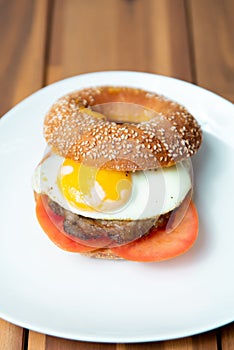 Vertical shot of a delicious bagel with beef, fried eggs and tomatoes in a white plate