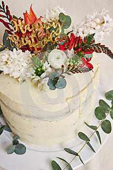 Vertical shot of a delicious birthday white cream flowers on the top cake with a drip on the side