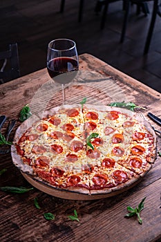 Vertical shot of a delicious cheesy pepperoni pizza with a glass of wine on a wooden table