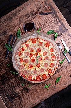 Vertical shot of a delicious cheesy pepperoni pizza with a glass of wine on a wooden table