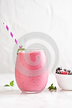 Vertical shot of a delicious mix berry milkshake with different berries in a bowl next to it