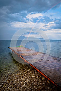 Vertical shot of distant rainbow over the wooden dock after heavy rainfall in Achaea, Greece