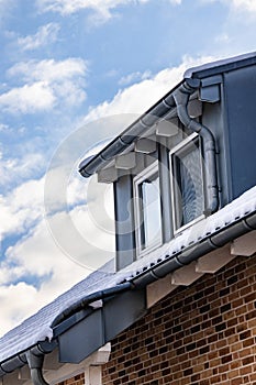 Vertical shot of dormer windows covered in the snow under a blue cloudy sky