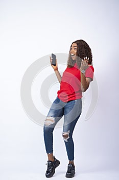 Vertical shot of an excited young African woman holding her phone looking happily towards her side